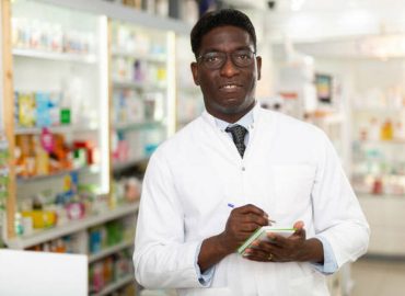African-american male pharmacist standing with notebook in hands in salesroom of drugstore